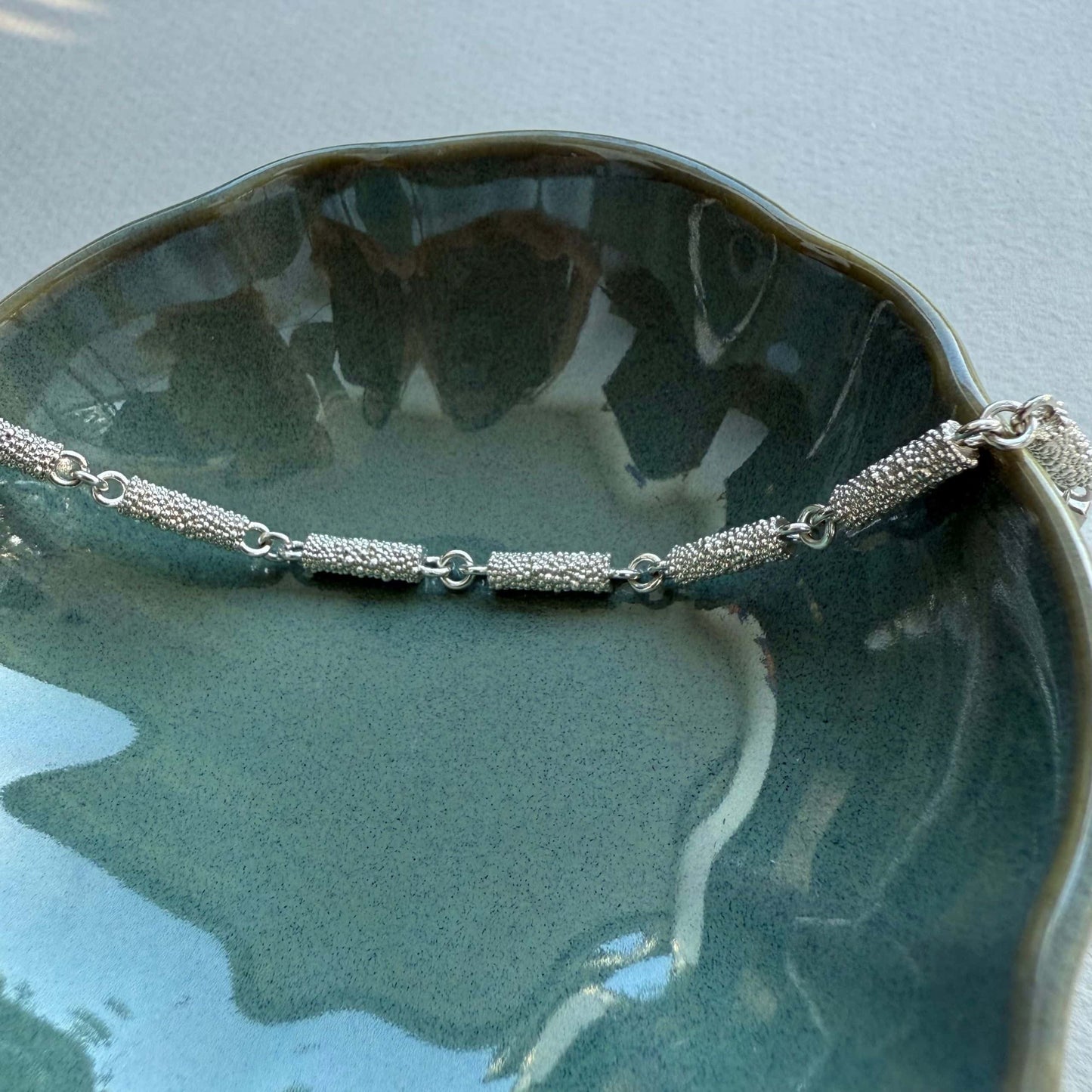 Fairmined Silber Armband mit texturierter Oberfläche, in Keramikschälchen liegend, stimmungsvolle Nahaufnahme