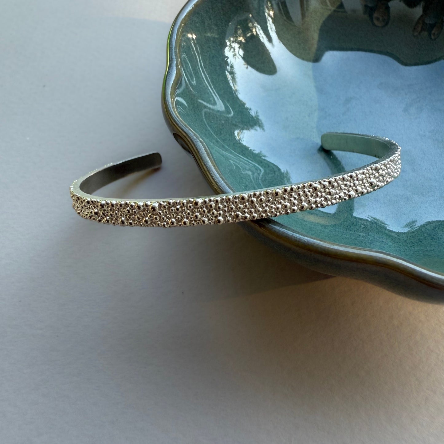 Offener, minimalistischer Fairmined Silber Armreif, arrangiert an kleinem Keramikschälchen bei natürlichem Licht