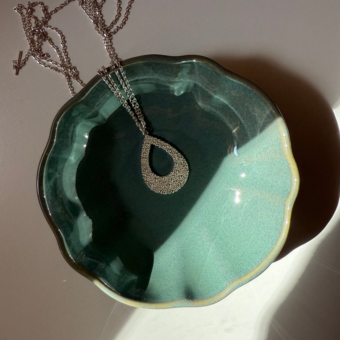 Fairmined Silber Halskette mit tropfenförmigem Anhänger aus kleinen Kügelchen, in kleinem Keramikschälchen mit stimmungsvollem Licht