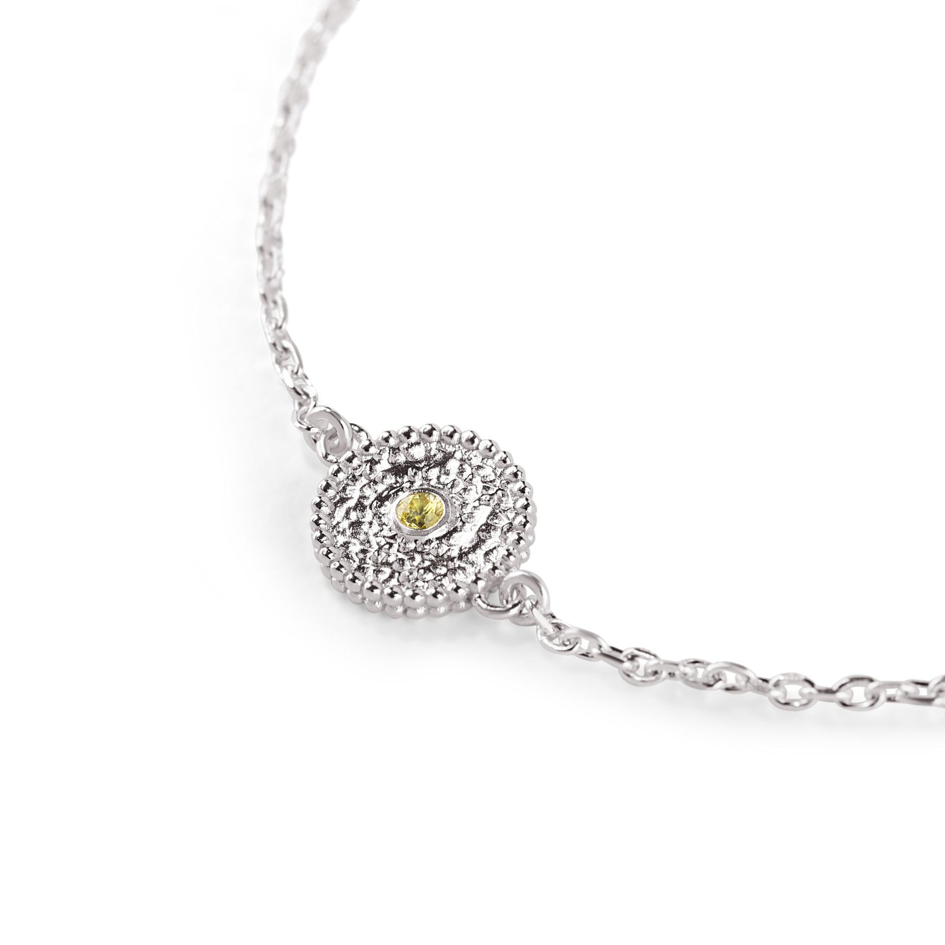 Nahaufnahme eines zierlichen Charms aus Fairmined Silber, am Rand mit kleinen Kügelchen verziert, mittig ein hellgelber fair gehandelter Saphir, freigestellt auf weißem Hintergrund