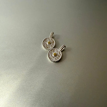 Zwei runde Anhänger aus Fairmined Silber mit hellgelbem, fair gehandeltem Saphir, nebeneinander liegend auf silbernem Untergrund bei natürlichem Licht